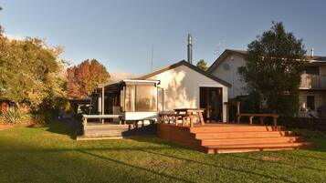 A residential property with a covered patio area, a wooden deck, and a small building with a chimney.