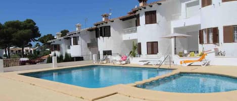 Un espace piscine avec une piscine à l’eau cristalline, des chaises longues et un bâtiment blanc doté de balcons.