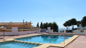 A swimming pool with a tiled deck, a view of the sea, and a building with a tiled roof in the background.