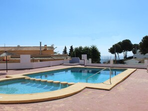 Une piscine avec une terrasse carrelée, une vue sur la mer et, au fond, un bâtiment doté d’un toit recouvert de tuiles.