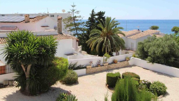 A coastal residential area with white buildings, a sandy courtyard, and a view of the sea.