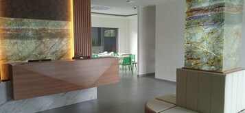 A reception area with a wooden reception desk, green chairs, and a large glass wall.