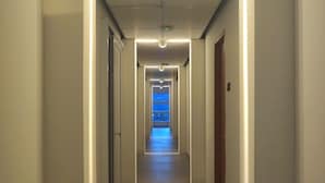 A long, narrow hallway with a central light fixture and a blue-lit exit at the end.