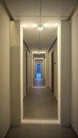 A long, narrow hallway with a central light fixture and a blue-lit exit at the end.