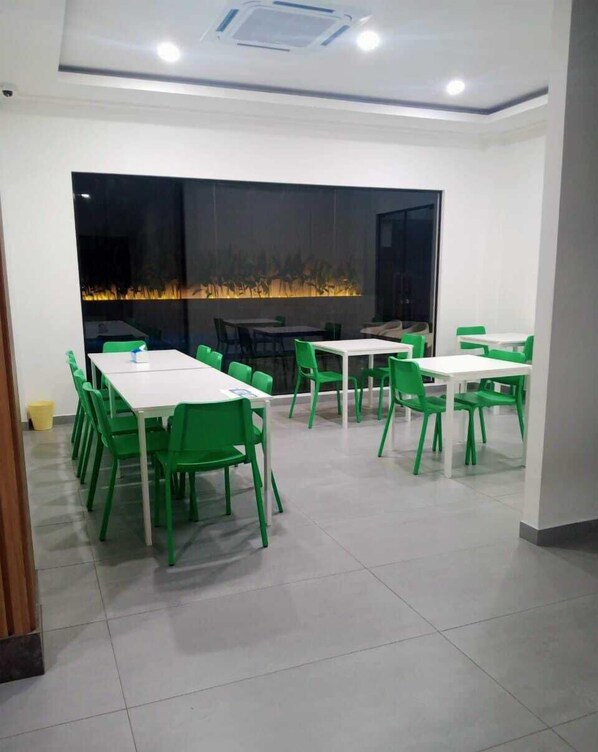 Un espace de restauration moderne avec des tables blanches et des chaises vertes, une grande fenêtre donnant sur un paysage urbain et un plafond doté d’un éclairage encastré.
