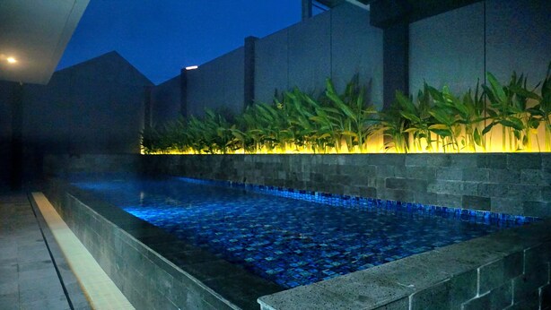 An indoor swimming pool with a tiled floor and a low wall with plants.