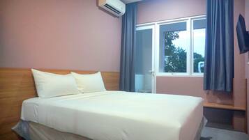 A hotel room with a bed, a window with curtains, an air conditioning unit, and a television on the wall.
