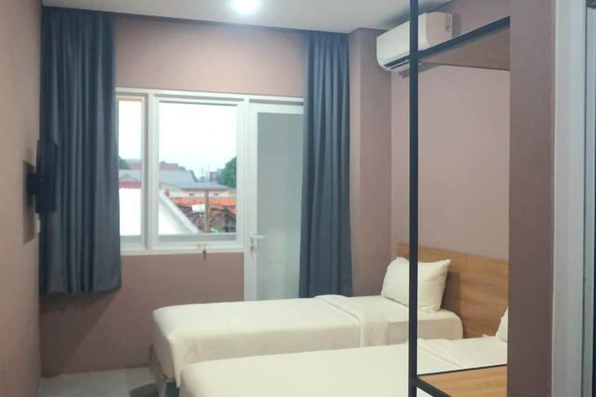 Une chambre d’hôtel avec deux lits, une fenêtre avec des rideaux, un appareil de climatisation et une vue sur les bâtiments environnants.