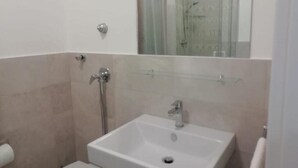 Un baño con un lavabo blanco, un espejo encima y una zona de ducha visible a través de la puerta de cristal.