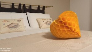 Una cama con ropa de cama blanca, almohadas decorativas, un cabecero de madera y un objeto geométrico naranja sobre la cama.