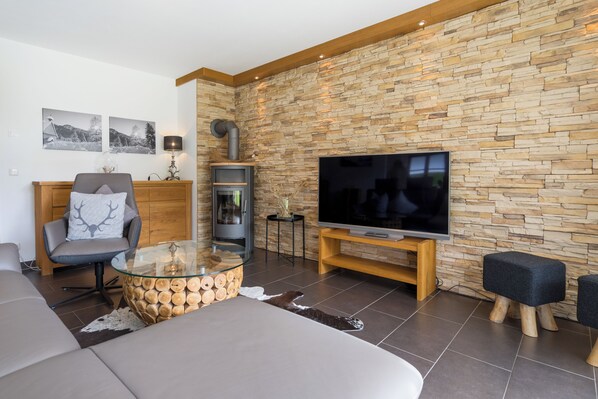 A modern living room with a stone wall, a fireplace, a TV, and a comfortable seating area.