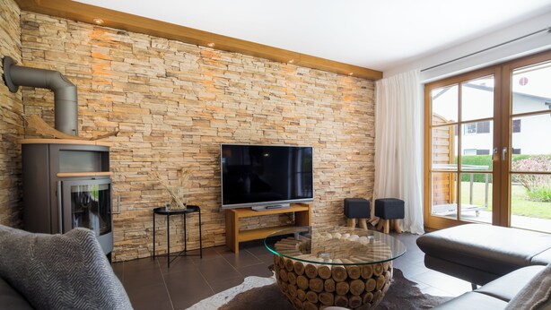 Una sala de estar moderna con pared de piedra, chimenea, televisor de pantalla plana y una mesa de centro de vidrio.