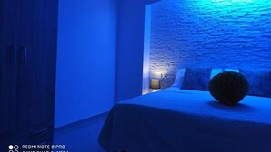 A room with a stone wall, a bed with a dark headboard, and a lamp on a bedside table.
