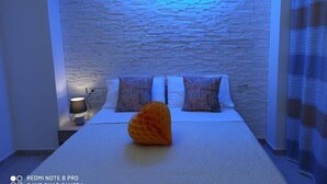A bedroom with a stone-textured wall, a bed with white bedding and patterned pillows, and a decorative orange object on the bed.