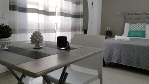A modern hotel room with a bed, a bedside table, a chair, a potted plant, and a window with curtains.