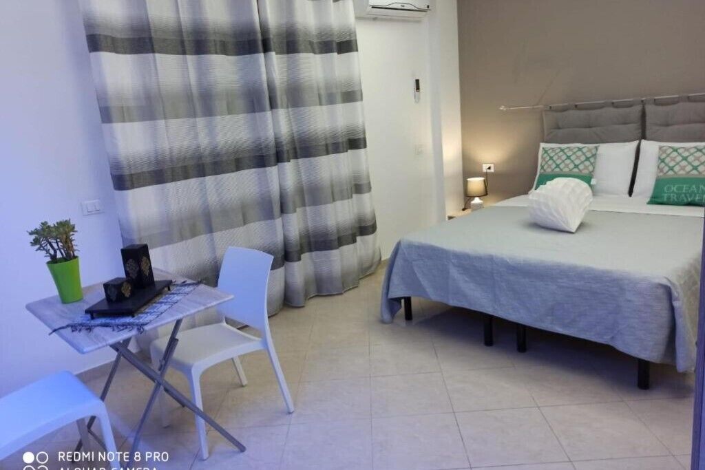 A hotel room with a bed, a desk, a chair, a potted plant, and a curtain.