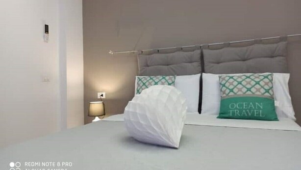 A hotel room with a bed, a nightstand, a lamp, and a wall-mounted air conditioner.