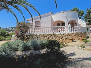 A Mediterranean-style villa with a stone wall, arched windows, and a white balcony railing. - Charming Villa in Moraira with Private Pool, Near Beach and Amenities, Pet-Friendly (Moravit)
