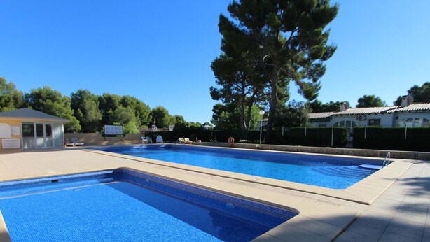A swimming pool with clear blue water, surrounded by a tiled deck and a building with a covered area. - Cozy Holiday Home in Moraira with Communal Pool, Near Golf & Beach, Perfect for Families (Moraira)