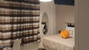A bedroom with a striped curtain, a bed with a white bedspread, an oval mirror, and a hanging light fixture.