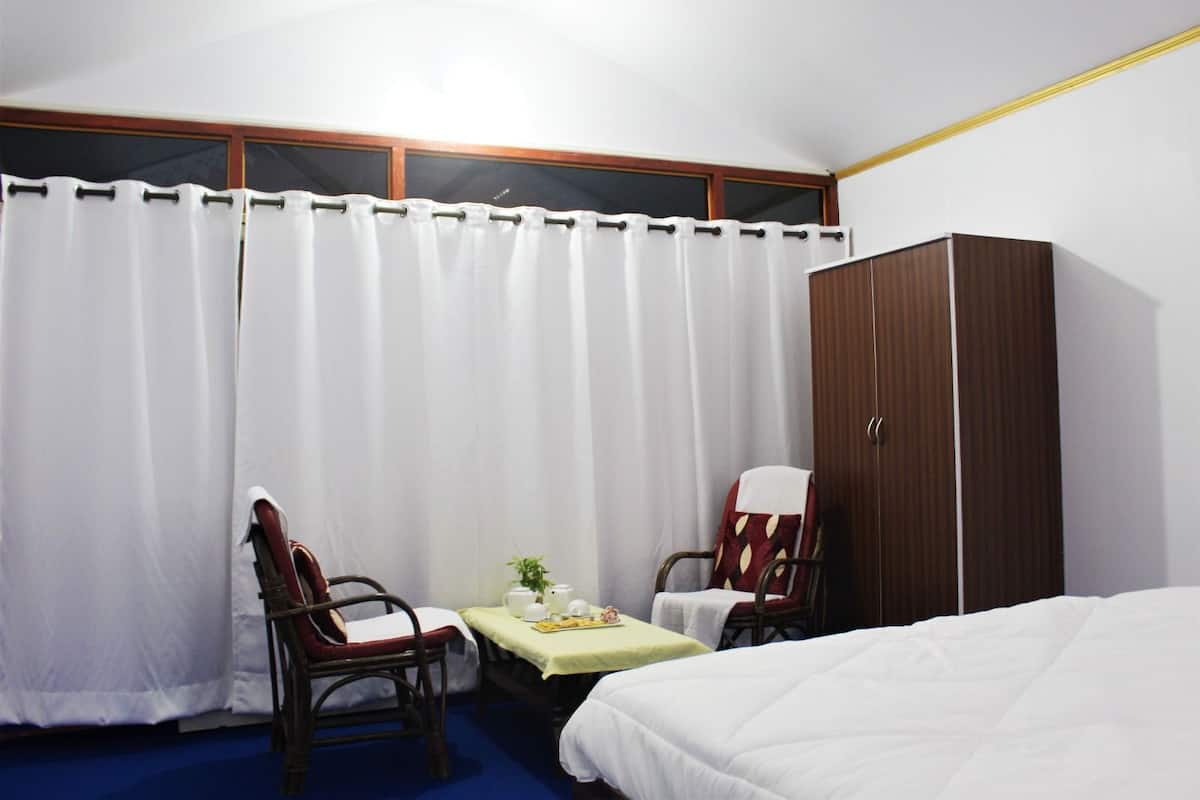 A hotel room with a bed, two chairs, a small table with tea set, and a wardrobe.