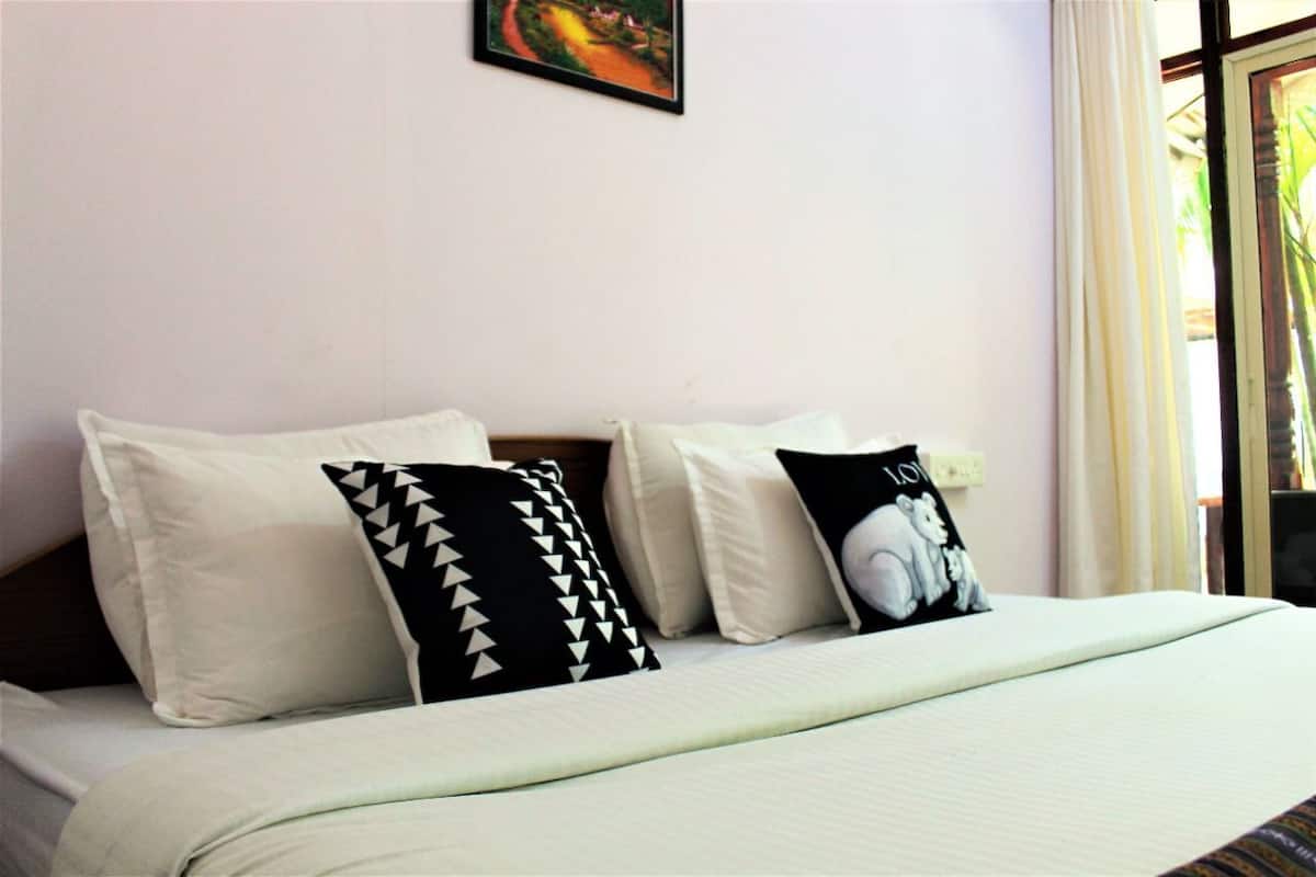 A bed with a white bedspread and three pillows, one with a black and white pattern, another with a black and white elephant design, and a plain white pillow.