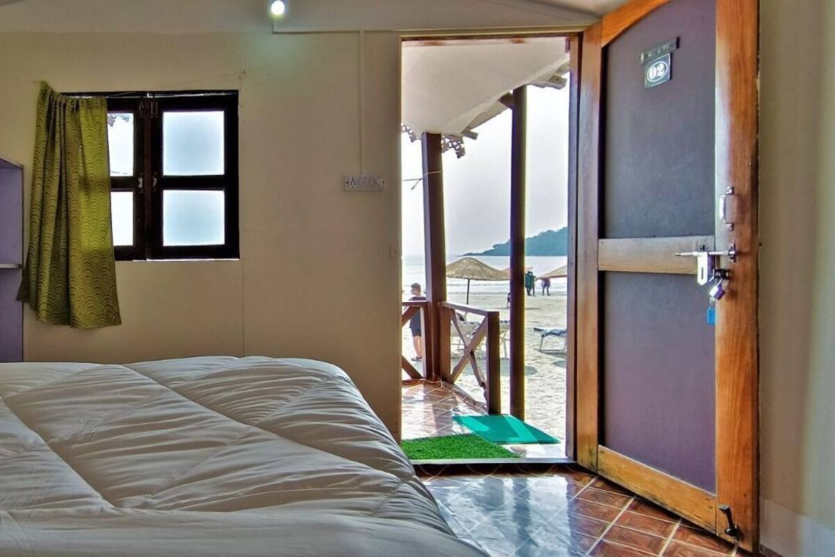 A room with a bed, a wardrobe, a window with curtains, and a door leading outside.