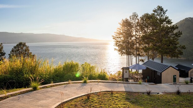Une vue sur le lac, avec un petit bâtiment, une zone pavée et de la verdure environnante.