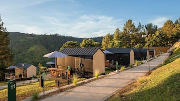 Una fila de cabañas con asientos al aire libre, un camino y vistas a un paisaje boscoso.