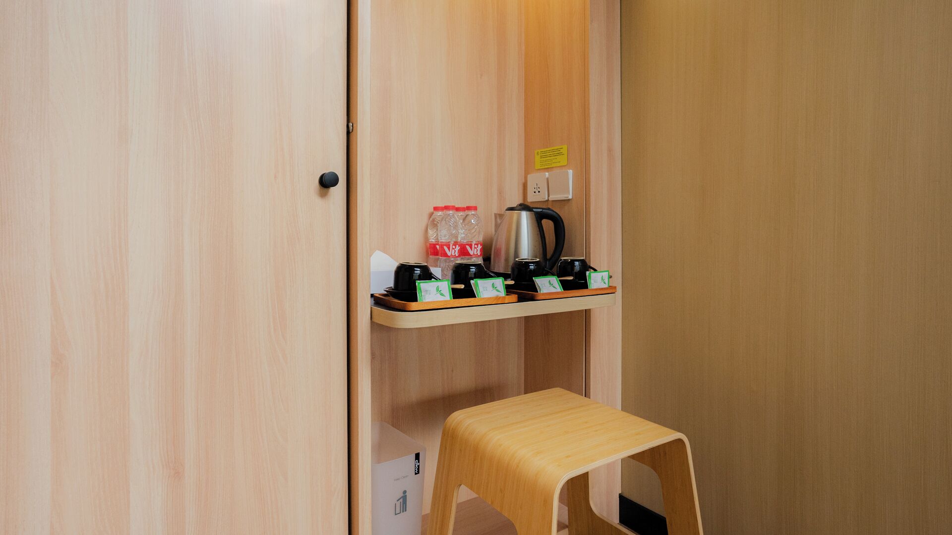 Ein Zimmer aus Holz mit einem Regal, auf dem ein Wasserkocher, eine Flasche und eine Tasse stehen.
