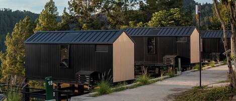 A row of cabins with a metal roof, positioned on a concrete path with a green sign indicating the number 18.