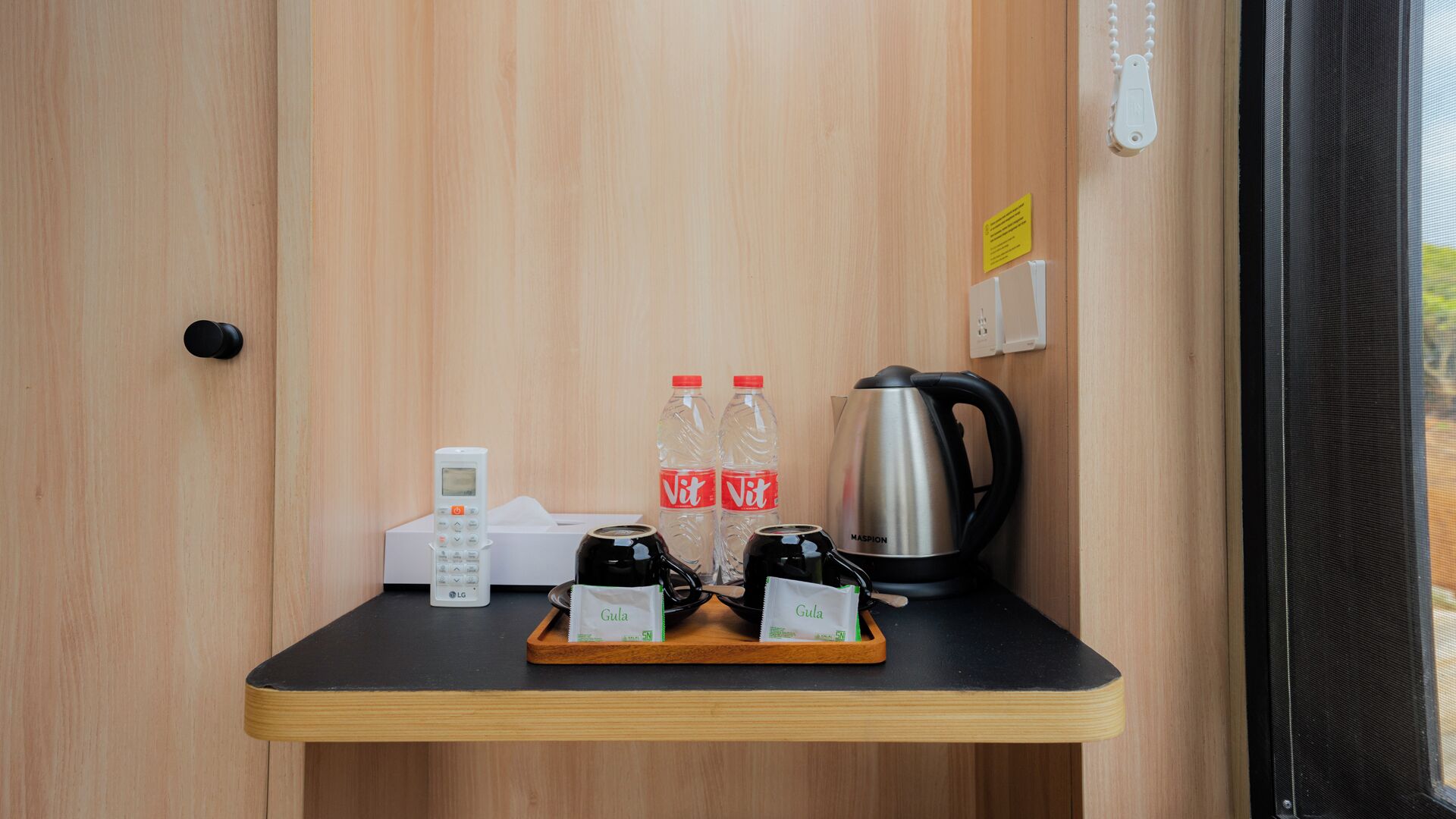 Interior de madera con una encimera negra que sostiene un teléfono, dos botellas de agua, una cafetera y dos saquetes de Gula.