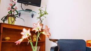 Un salon avec un canapé bleu, un coussin rouge, un meuble en bois et un vase rempli de fleurs.