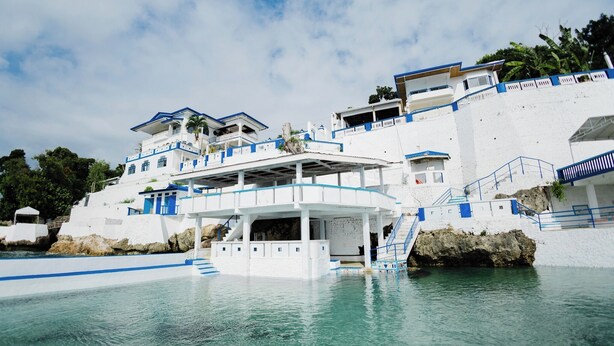 A white building with blue accents, a pool, and a staircase leading to the upper levels.