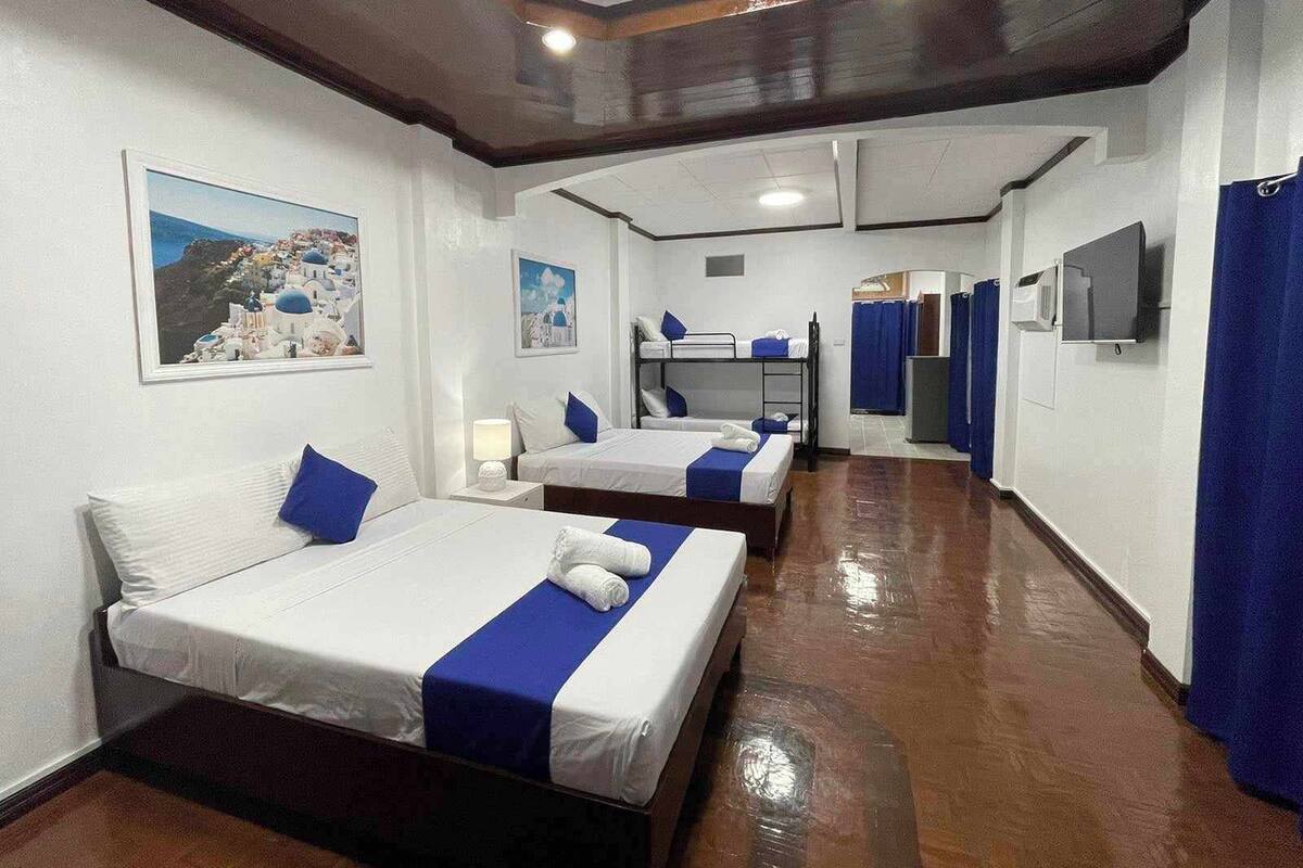 A hotel room with two beds, a bunk bed, a television, a mirror, and a bathroom with a shower curtain.