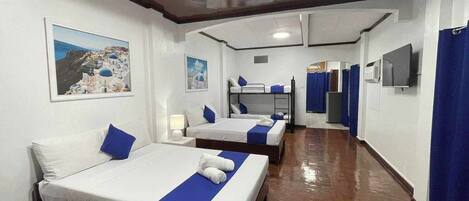 Habitación de hotel con dos camas, una litera, un televisor, un espejo y un baño con cortina de ducha.