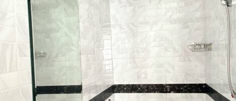 Casa de banho com azulejos de mármore branco, moldura preta e branca, cabine de duche com vidro, sanita branca e lavatório com torneira.