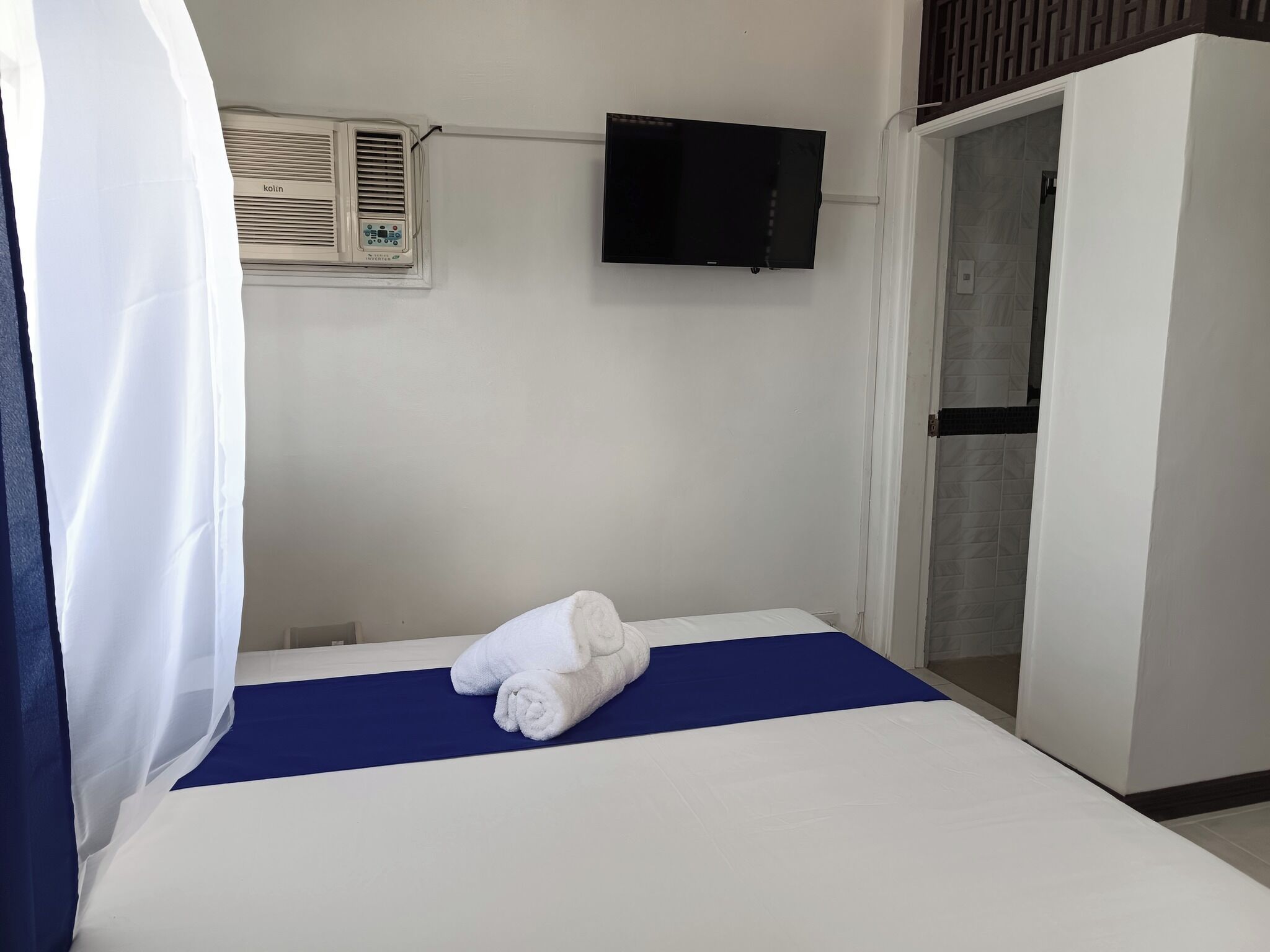 A hotel room with a bed, a television mounted on the wall, and a wardrobe.