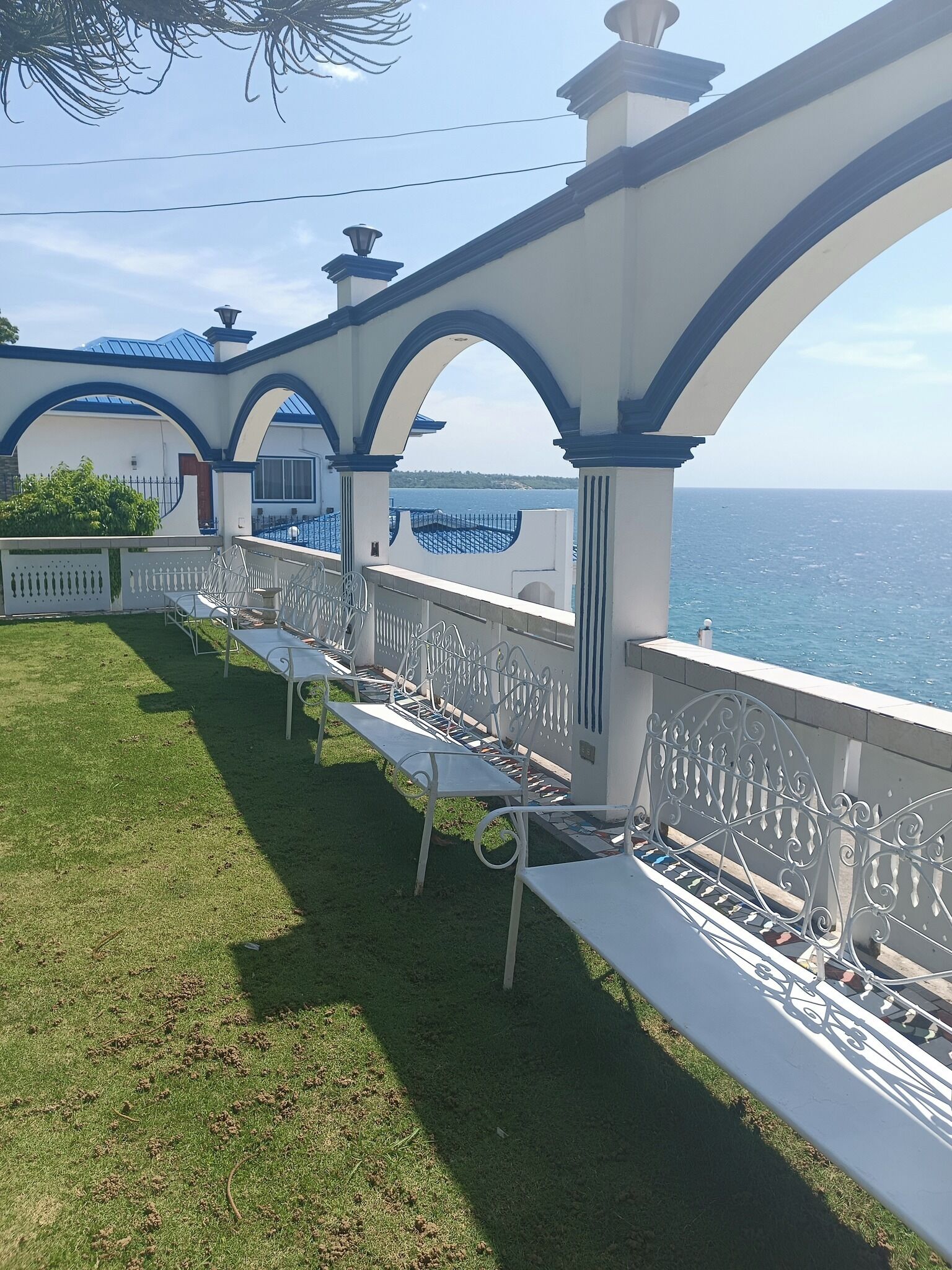 A seaside terrace with white benches and blue arches, overlooking the sea.