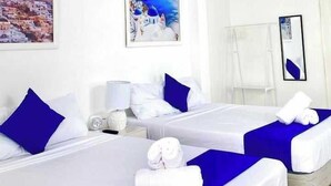 A hotel room with two beds, white bedding, blue accents, a painting of a coastal scene, a mirror, and a ceiling light.