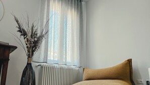 A room with a radiator, a brown cushion, and a vase with dried plants.