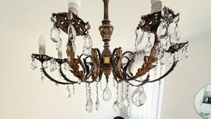 A dining area with a glass table, white chairs, a chandelier, and a wooden floor.