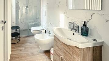 Een moderne badkamer met een marmeren spatwand, twee wasbakken, een bidet en een houten wastafelmeubel.