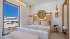A modern hotel room with a large bed, a wooden headboard, a round decorative wall piece, a hanging light fixture, and a view of a building through a large window.