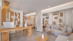 A modern living room with a wooden dining table, a sofa, and a coffee table. There is a lamp on the table and a wall with abstract designs.