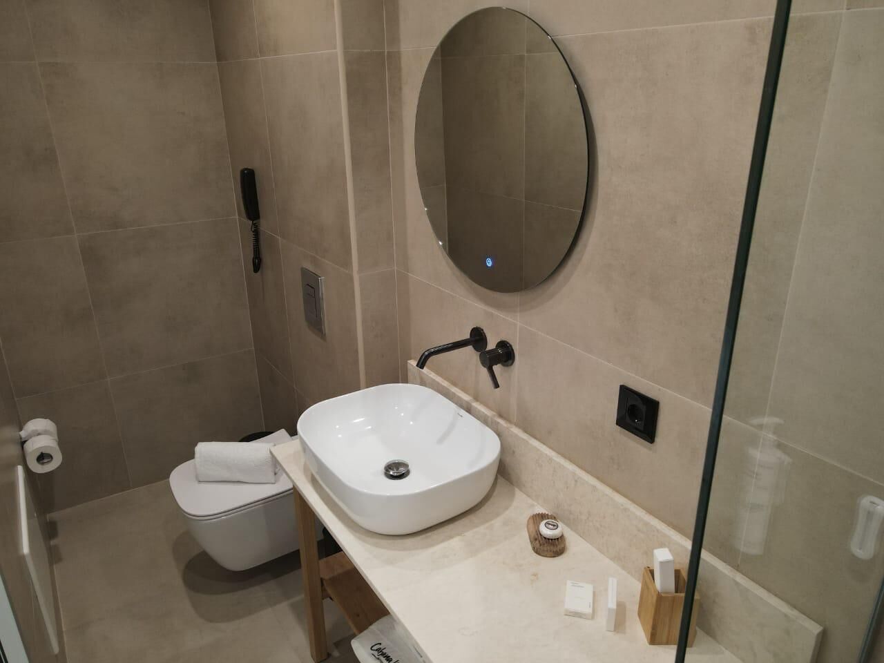 Un baño moderno con un lavamanos blanco, un espejo redondo y un inodoro.