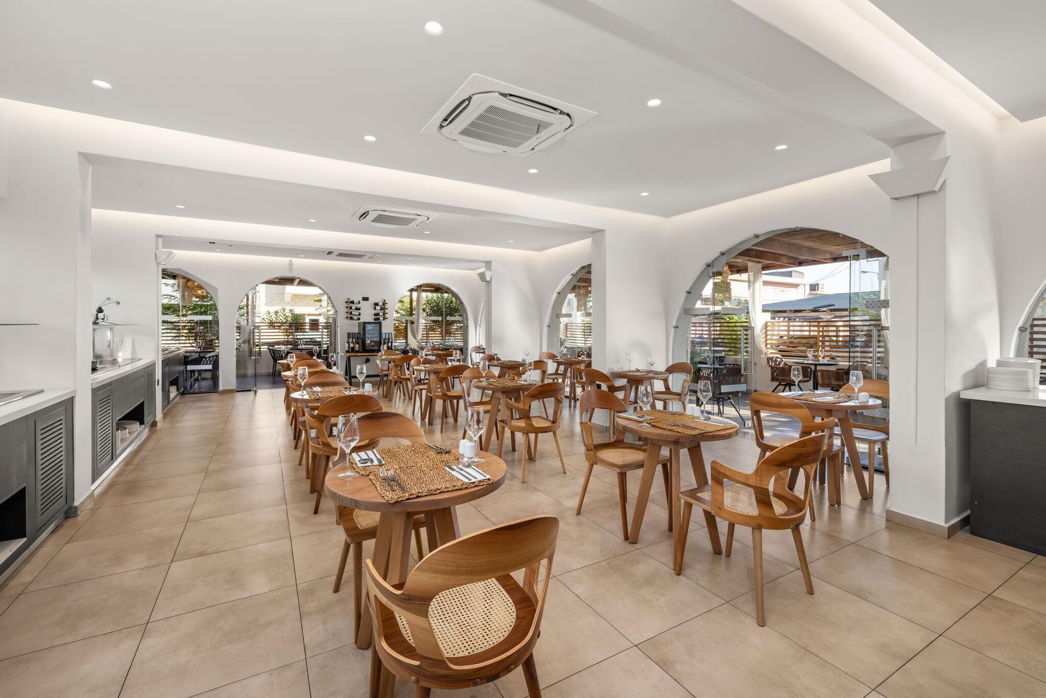 A spacious dining area with wooden tables and chairs, white walls, and large windows allowing natural light.