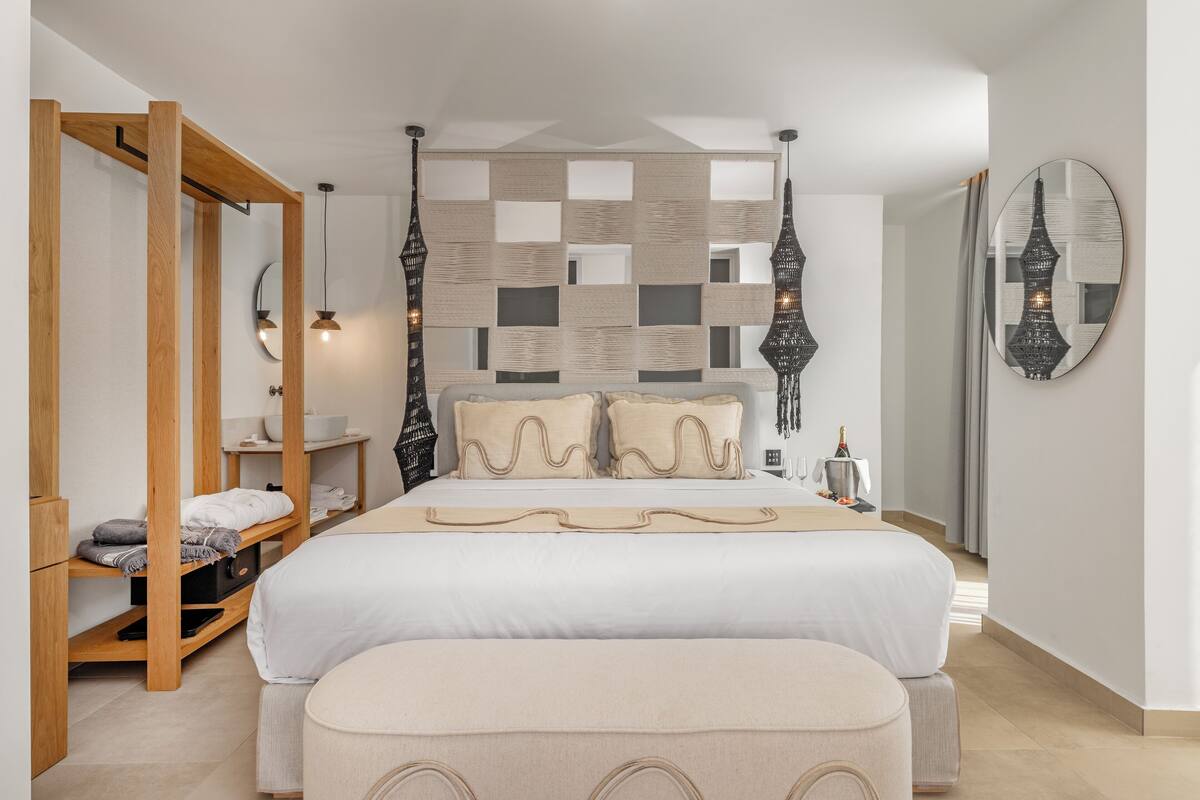 A modern bedroom with a large bed, wooden shelving, a mirror, and hanging lights.