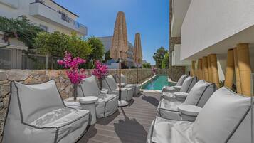 Una terraza en la azotea con mobiliario exterior, una piscina y vistas a un edificio alto.