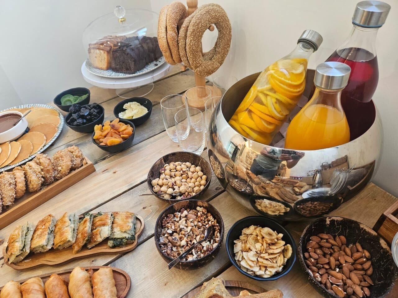 Une variété d’aliments, notamment des pâtisseries, des fruits à coque et des boissons, sont disposés sur une table en bois.